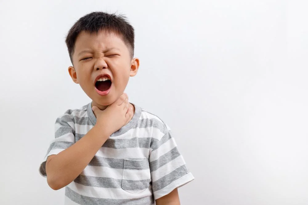 Child holding neck with mouth open showing throat discomfort