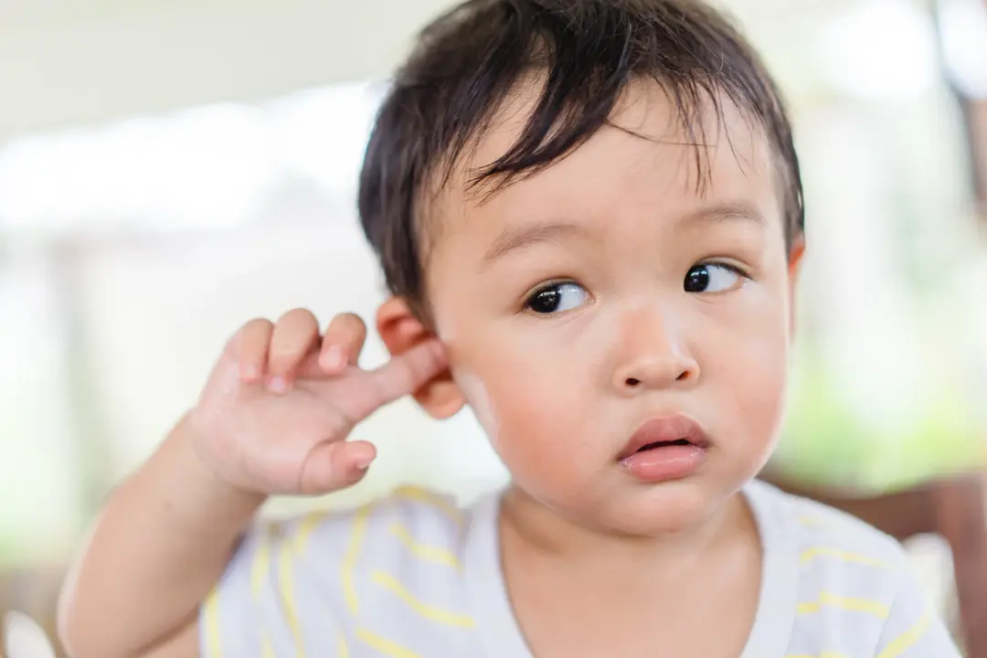 Child touching ear with finger while looking to the side