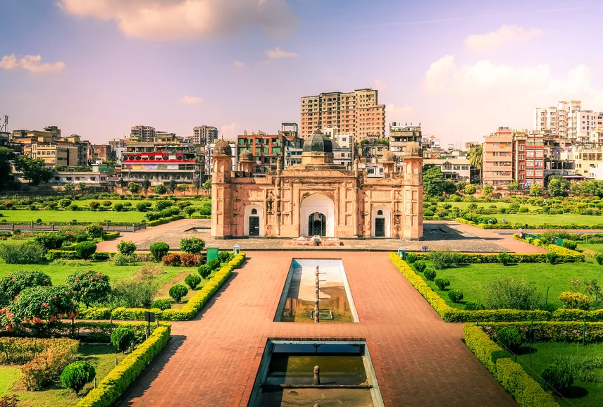 Mughal-era mosque in a landscaped garden with reflecting pools, set against a modern city skyline.