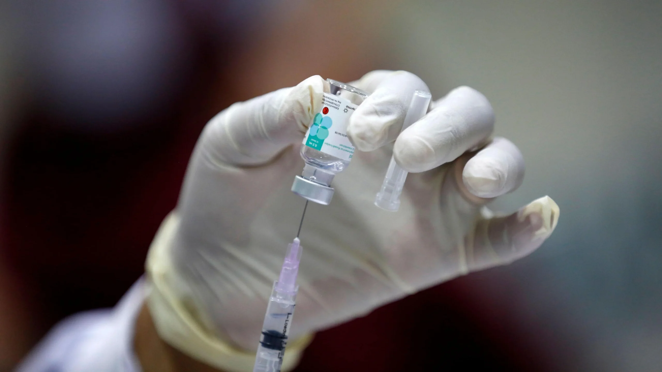 Gloved hand preparing vaccine syringe from vial at Yatton Pharmacy in Yatton, Bristol