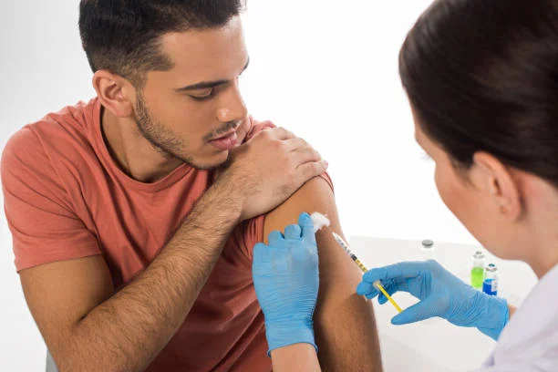 A healthcare professional wearing blue gloves administers an injection to a patient’s upper arm at Yatton Pharmacy, Yatton, Bristol.