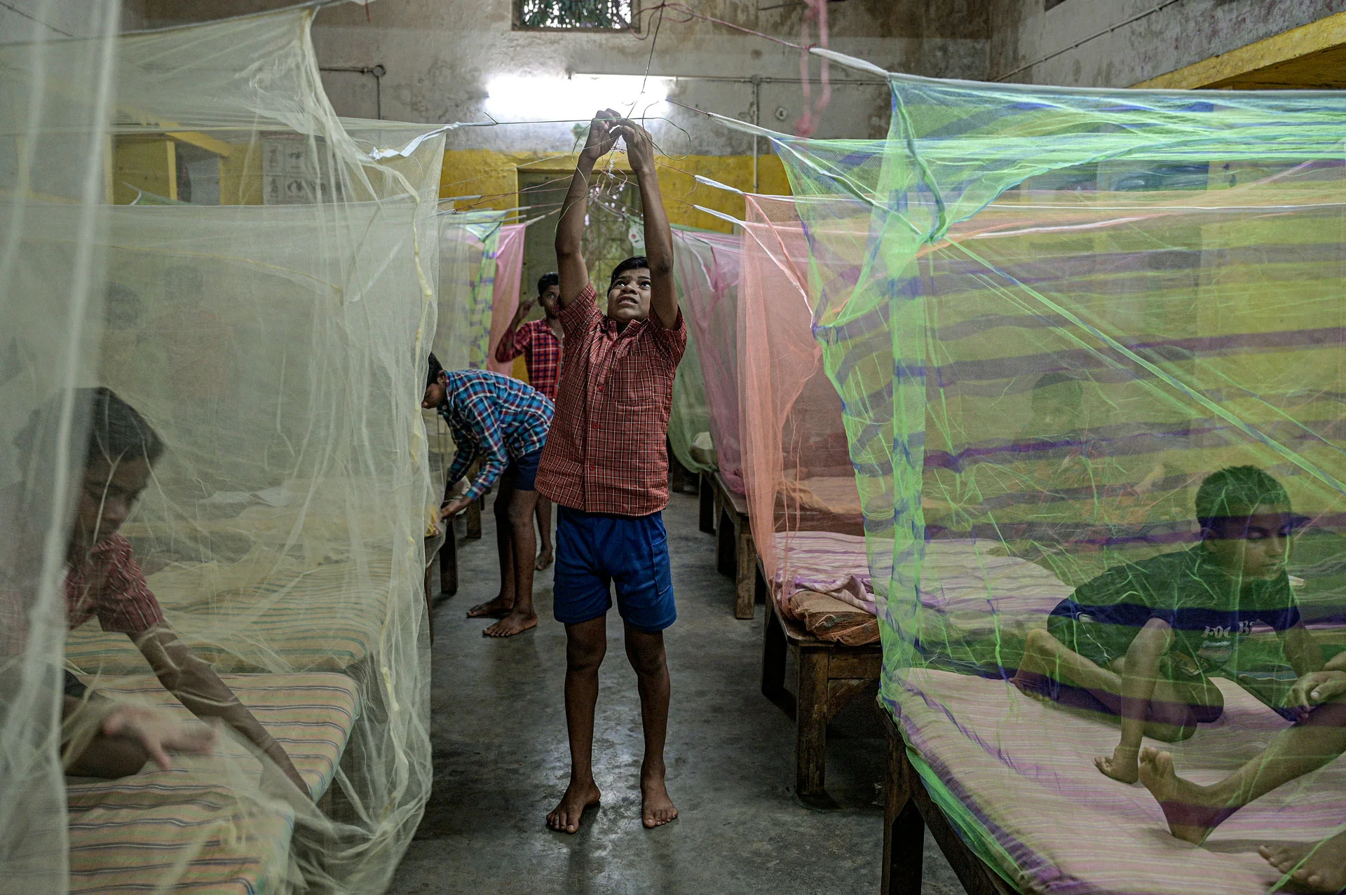 Children in a dormitory preparing colorful mosquito nets over beds as protection against Maleria.