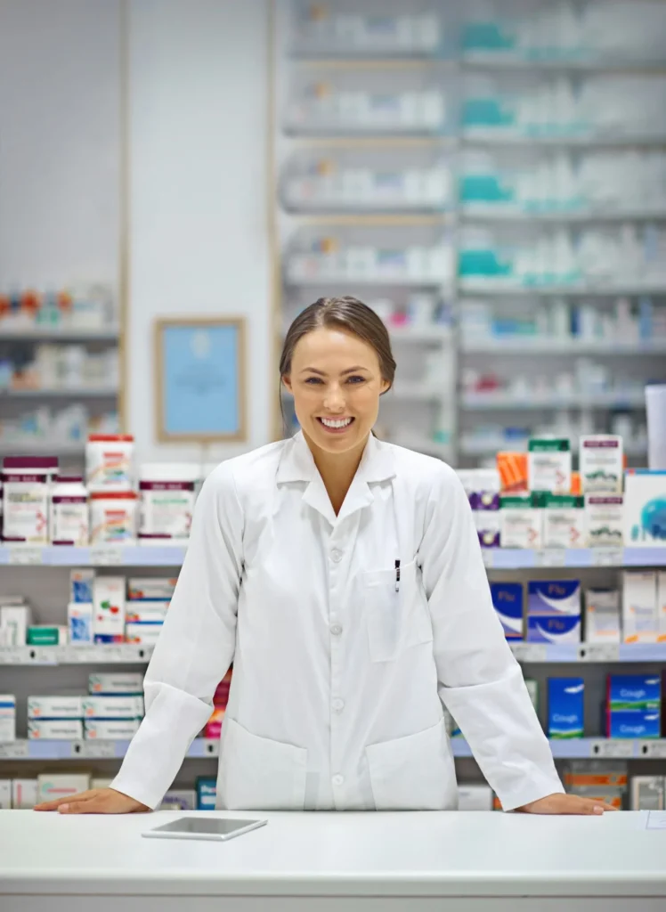 A pharmacist in a white lab coat stands behind the counter with shelves of medications at Yatton Pharmacy, Yatton, Bristol.
