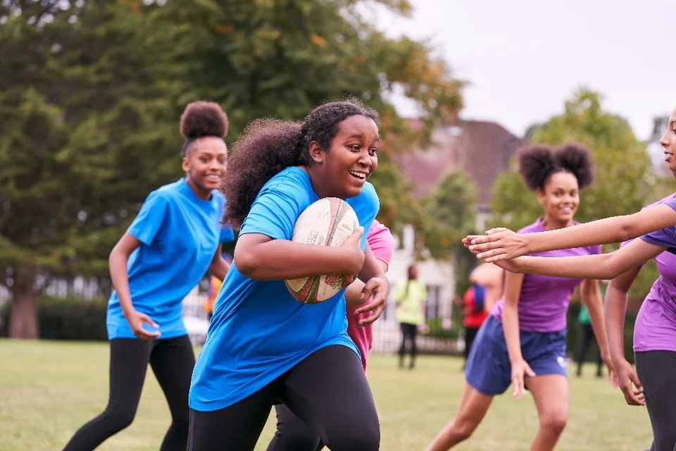 Young people playing rugby outdoors on grassy field at Yatton Pharmacy in Yatton, Bristol